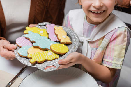 cropped view of smiling girl holding tray with colorful easter cookies