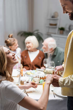 smiling woman holding hand of husband pouring wine during easter dinner
