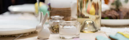 selective focus of decorative rabbit and candle on table served for easter dinner, banner
