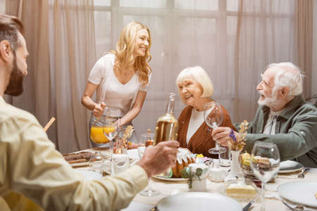 smiling woman pouring orange juice near senior parents during easter celebration