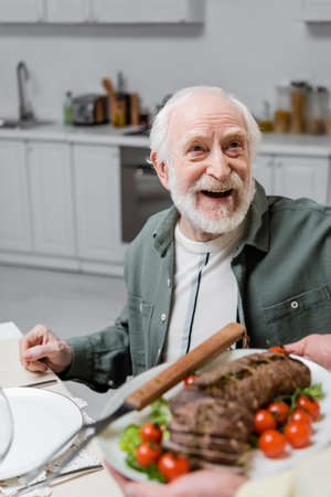 amazed senior man looking at wife holding plate with meat during easter celebrationの写真素材