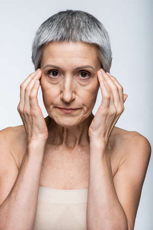 middle aged woman with bare shoulders and wrinkles isolated on grayの写真素材