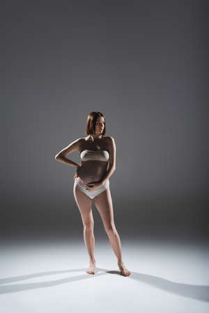 Pregnant woman in underwear touching belly on grey backgroundの写真素材