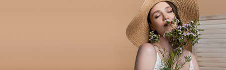 Woman in straw hat holding flowers near face isolated on beige, bannerの写真素材