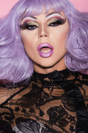 portrait of eccentric man with bright makeup and open mouth looking at camera isolated on pinkの写真素材