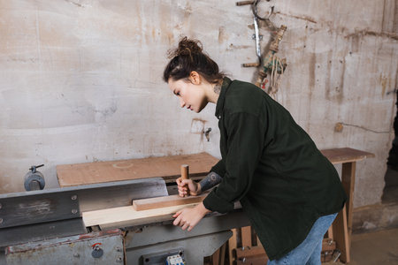 Side view of carpenter working with plank and jointer machine in workshopの写真素材