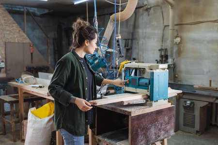 Side view of brunette carpenter turning on thickness planer in workshop