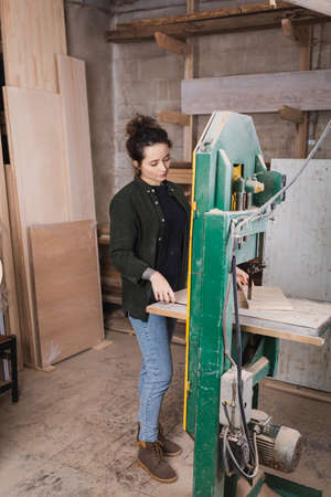 Carpenter holding wooden plank while working on band saw in workshop
