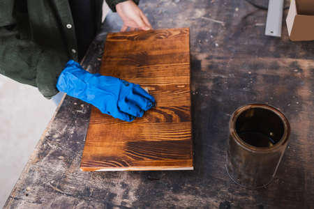 Top view of woodworker applying wood stain on board near jar in workshopの写真素材