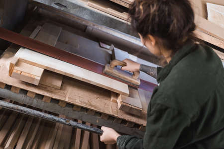 High angle view of tattooed furniture designer polishing wooden plank in workshop