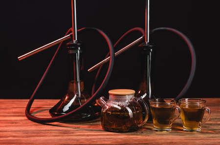 Teapot near hookahs on wooden table isolated on black