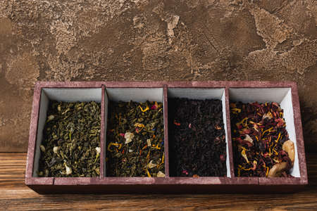 Top view of dry tea in box on wooden surface on textured stone background