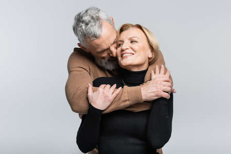 Gray haired man kissing and hugging wife isolated on grayの写真素材