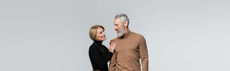 Smiling mature woman touching bearded husband isolated on grey, banner