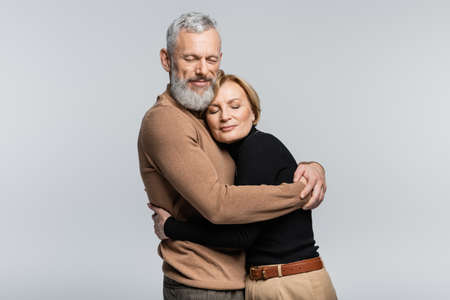 Bearded gray haired man hugging wife with closed eyes isolated on grayの写真素材