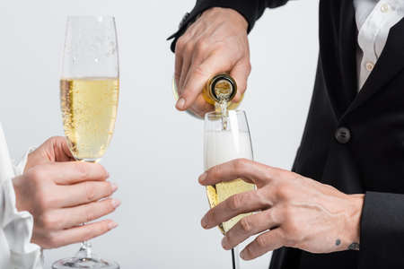 Cropped view of groom pouring champagne near bride with glass isolated on grayの写真素材