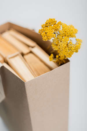 selective focus of dried yellow flowers near blurred shopping bag with books isolated on grayの写真素材