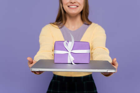 cropped view of happy young woman holding laptop with gift box isolated on purpleの写真素材