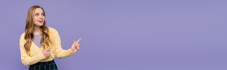 joyful young woman pointing with fingers isolated on purple, bannerの写真素材