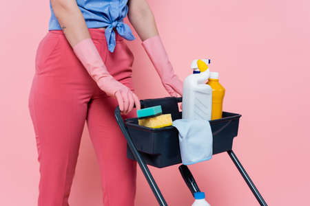 cropped view of tattooed woman in rubber gloves standing near housekeeping cart with cleaning...