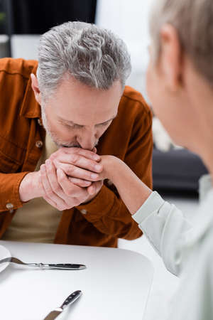 Mature man kissing hand of blurred wife in kitchen