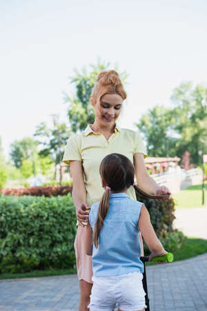 smiling woman touching hair of daughter while standing outdoorsの写真素材