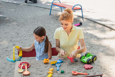 smiling woman with daughter playing with toys and sand outdoors