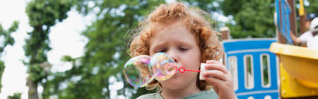 boy blowing soap bubbles outdoors in park, banner