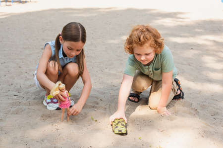 full length view of kids playing with doll and armored vehicle on sand outdoorsの写真素材
