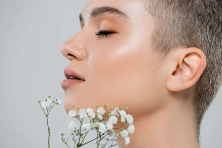 profile of charming woman with perfect face near white tiny flowers isolated on greyの写真素材