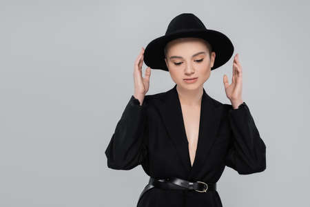 trendy woman with natural makeup touching black brim hat isolated on greyの写真素材