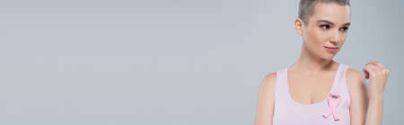 young woman with short hair and pink awareness ribbon on tank top isolated on grey, bannerの写真素材