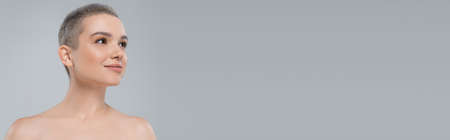 charming woman with naked shoulders and natural makeup looking away isolated on grey, bannerの写真素材