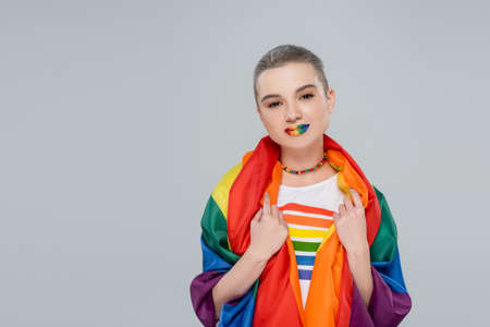 young and pretty woman with lgbt flag on shoulders looking at camera isolated on greyの写真素材