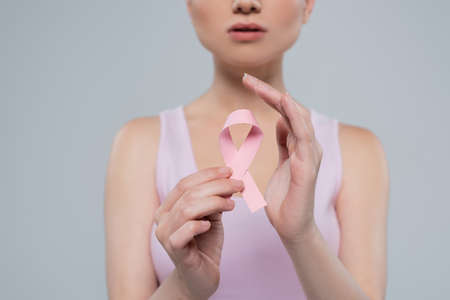 cropped view of blurred woman holding pink awareness ribbon isolated on greyの写真素材