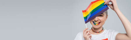 happy woman obscuring face with small lgbt flag isolated on grey, bannerの写真素材