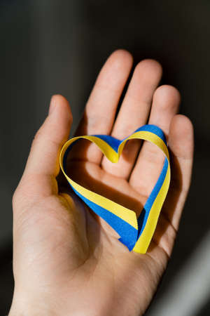 Cropped view of blue and yellow ribbon in heart shape on male hand on dark grey backgroundの写真素材
