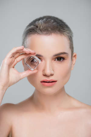 young woman with perfect skin holding ice cube near face isolated on greyの写真素材