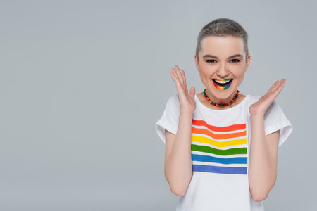cheerful woman in rainbow color t-shirt looking at camera isolated on grey