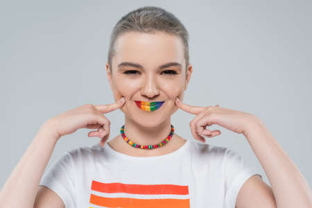 cheerful woman with rainbow colors lips touching cheeks isolated on greyの写真素材