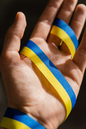 Cropped view of blue and yellow ribbon on blurred male hand on black backgroundの写真素材