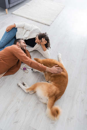 top view of joyful young couple looking at each other while lying of floor with akita inu dogの写真素材