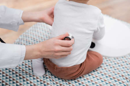 Cropped view of family doctor examining back of baby boy on medical couch in clinicの写真素材