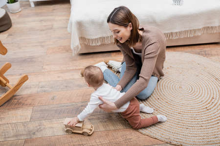 High angle view of smiling mother holding baby boy with toy car in bedroom