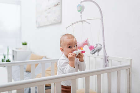 Baby boy biting toy in crib at home
