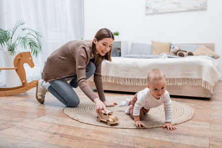 Happy young woman playing with toy car near baby son at home