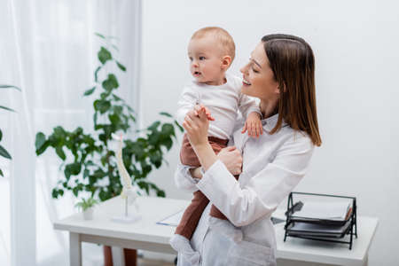 Young family doctor holding hand of baby boy in clinicの写真素材