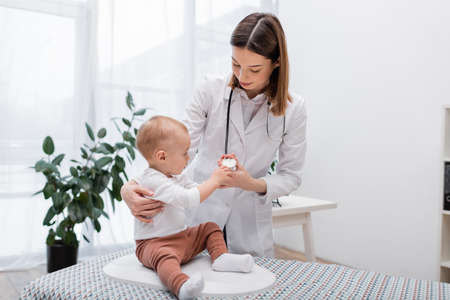 Baby touching stethoscope on doctor while sitting on electronic scale in clinicの写真素材