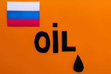 Top view of russian flag, oil lettering and paper drop on orange background, war in ukraine concept