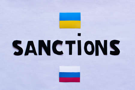 Top view of sanctions lettering near ukrainian and russian flags on white backgroundの写真素材